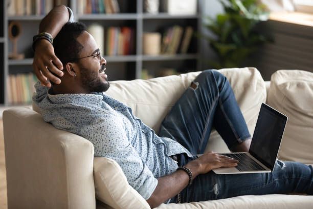 istock Dreamy smiling African American man lying on couch with laptop 1270851194
