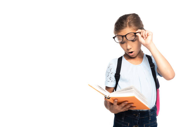 istock shocked schoolgirl touching glasses while reading book isolated on white 1270853256