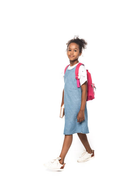 african american schoolkid patrząc na kamerę podczas chodzenia izolowane na białym - schoolgirl child backpack book bag zdjęcia i obrazy z banku zdjęć