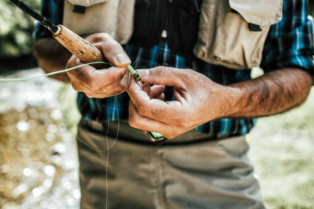Fly Fishing Close up shot of senior fisherman's hands tying a fly for fishing. Fly fishing concept. View from above. High angle view over shoulder. hook equipment stock pictures, royalty-free photos & images