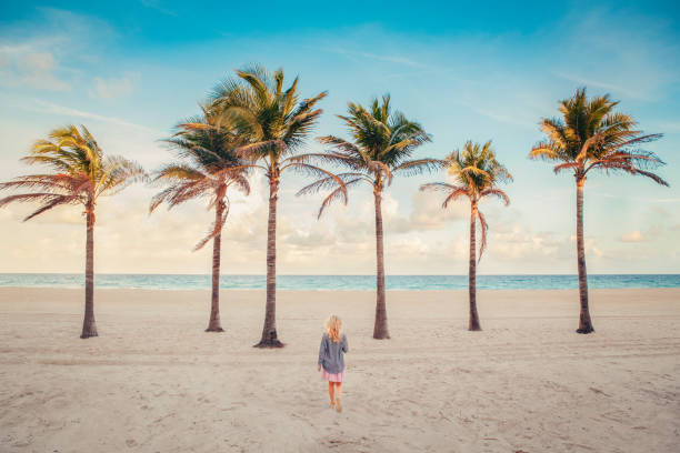 Little blonde Caucasian girl walking on empty Hollywood ocean beach in Florida. Child among tall palm trees on summer sunny day at sunset. View from back. Travel vacation kid holiday concept. Little blonde Caucasian girl walking on empty Hollywood ocean beach in Florida. Child among tall palm trees on summer sunny day at sunset. View from back. Travel vacation kids holiday concept. hollywood florida photos stock pictures, royalty-free photos & images