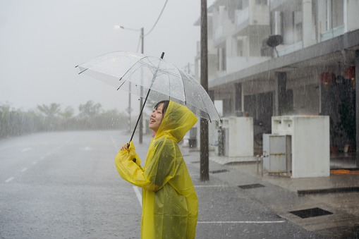 Shot of an Asian Chinese woman holding umbrella wearing raincoat and enjoying the rainy day