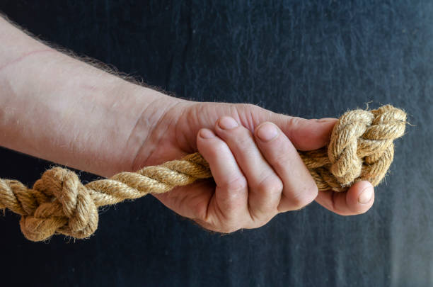 istock A man's hand holds a rope with a knotted knot on a dark background. 1270893918