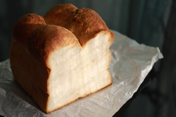 Stock photo featuring a sliced white bread loaf/loaves, symbolizing the essence of UPF ultra-processed food, set against a background of turquoise blue. The loaf of white is showed on its end, with the slices neatly arranged.
