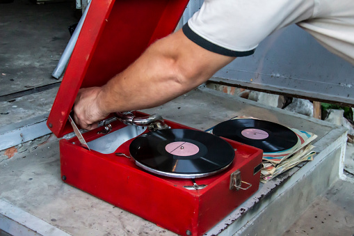 Old red vintage record player with vinyl record outside house. A hand of man turn on a record player. Old school style.