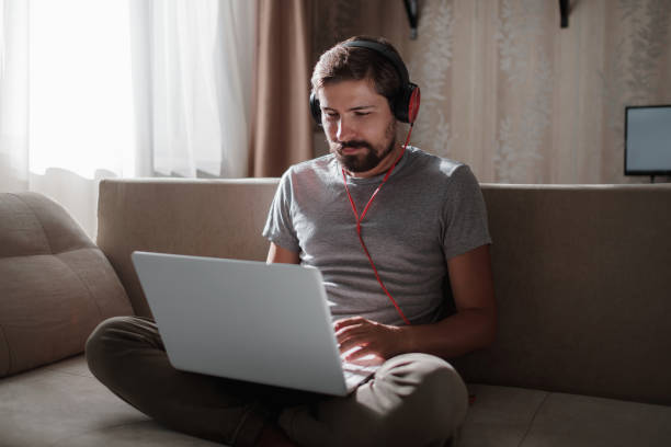 istock Man on sofa with headphones and notebook at home 1270906837