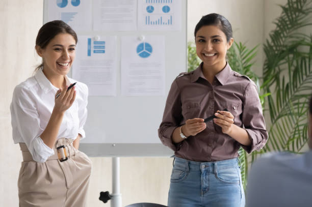 two happy mixed race female colleagues presenting marketing research results. - indian ethnicity audio imagens e fotografias de stock