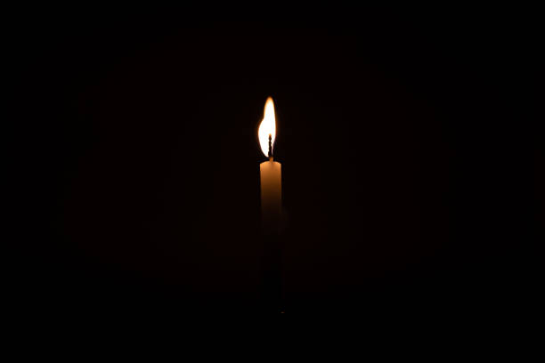 istock Close up single burning, bright white paraffin candle light on isolated dark black background. Red, orange, yellow candle fire flame smoke in party festival celebration at night. Copy space for text. 1270914895