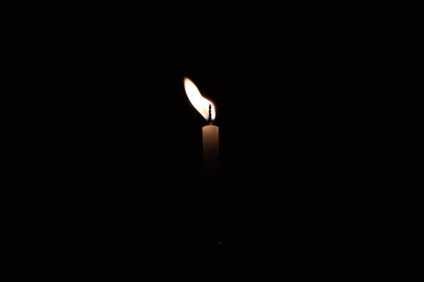 istock Close up single burning, bright white paraffin candle light on isolated dark black background. Red, orange, yellow candle fire flame smoke in party festival celebration at night. Copy space for text. 1270914912