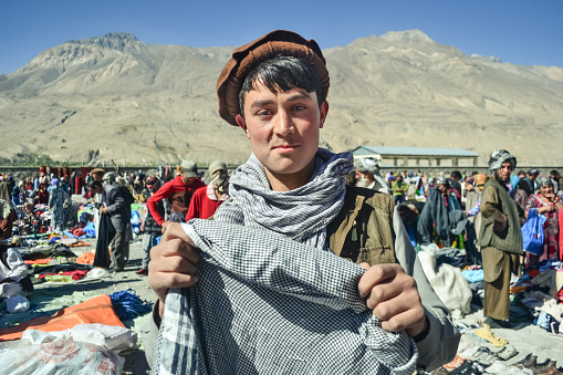 Ishkashim / Afghanistan - October 5, 2013: Handsome Afghan Pashtun young man smiles holding head scarf in Afghan market between Tajikistan and Afghanistan