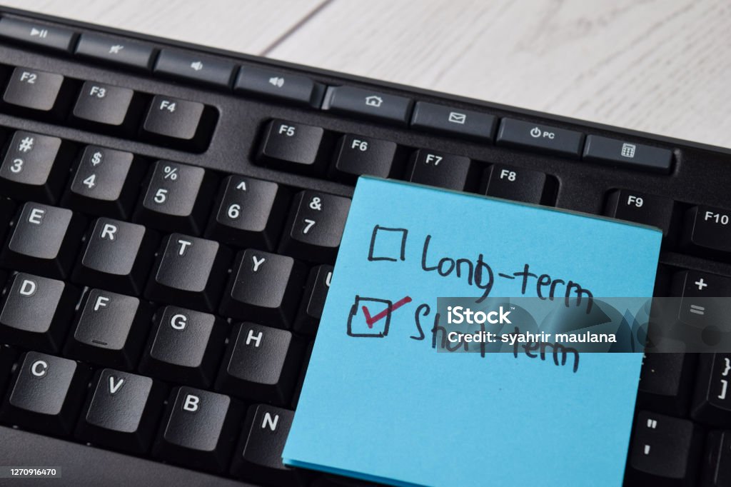 Long-term and Short-term write on a sticky note. Supported by an additional services isolated wooden table. Short - Length Stock Photo