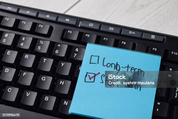Longterm And Shortterm Write On A Sticky Note Supported By An Additional Services Isolated Wooden Table Stock Photo - Download Image Now