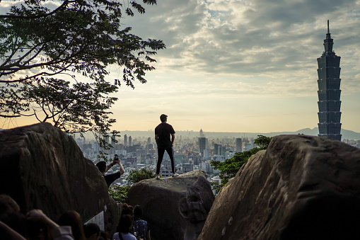 Taipei / Taiwan - December 12, 2018: silhouette of young man posing on rock with view of Taipei 101 skyscraper and Taipei cityscape from Elephant Mountain