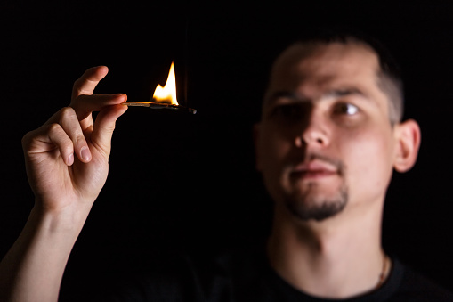 Dramatic dark portrait of man looking at lit fire of a match