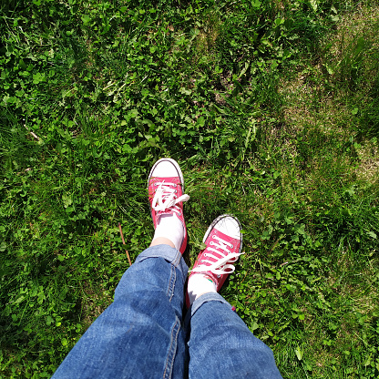 Top view of the feet of a girl in red sneakers on green grass on a bright sunny day the sun's rays summer fun