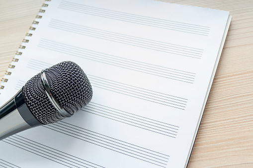 Microphone on a blank musical white sheet close up. Singing, writing music, karaoke online, creativity, vocals concept, symbol. Singing lessons