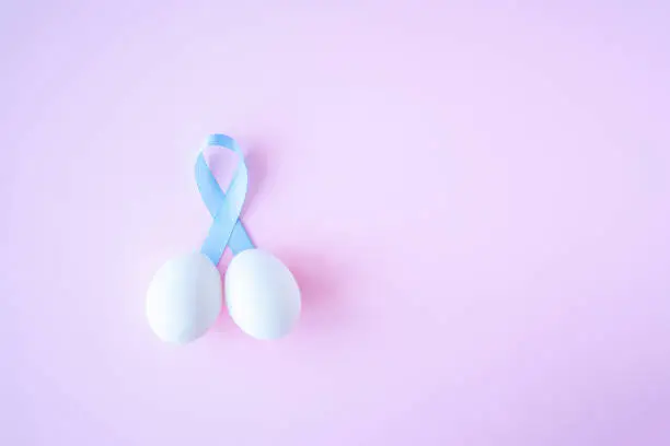 prostate cancer, healthcare, profession, medicine concept - close up of chicken white eggs and blue ribbon in penis shape on bright background. Cancer awareness, cure, men carcinoma