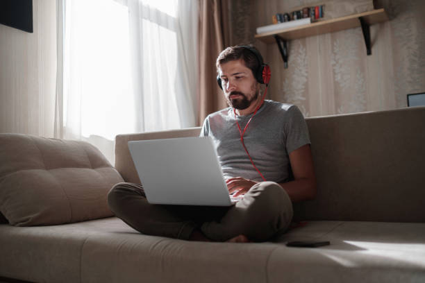 istock Man on sofa with headphones and notebook at home 1270923484