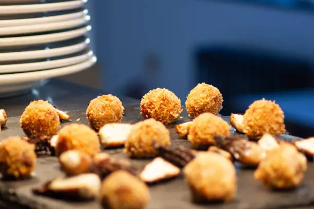 deep fried arancini balls in restaurant kitchen on blue background with stack of white plates