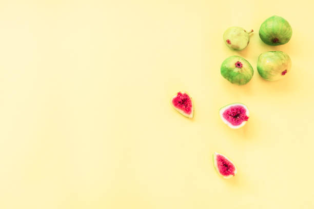 Whole green figs and sliced on a yellow background, flat lay, copy space