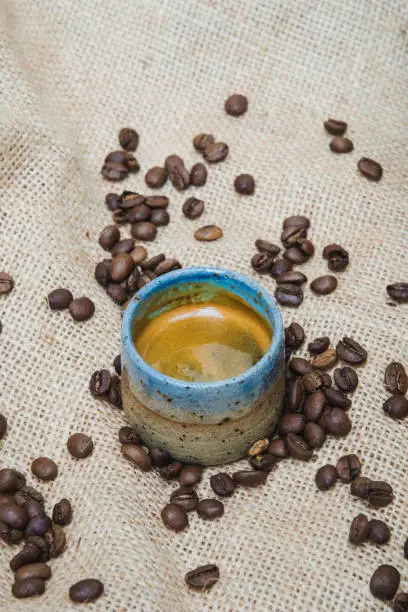 espresso coffee in blue beige natural stone ceramic mug with dark roasted coffee beans on hessian fabric background