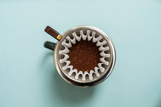 ground coffee in filter on blue background overhead shot of dark ground coffee beans in coffee filter on pale blue background coffee filter stock pictures, royalty-free photos & images