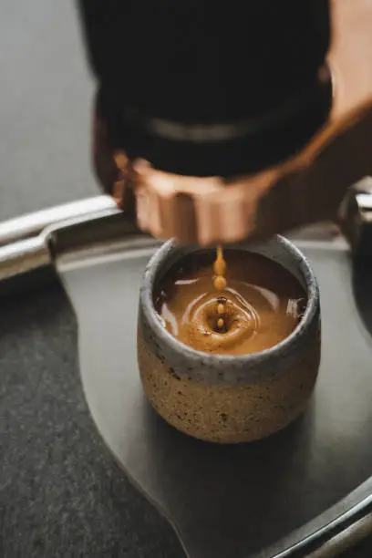 close up soft focus portrait shot of espresso dripping into crema from manual espresso machine into ceramic mug