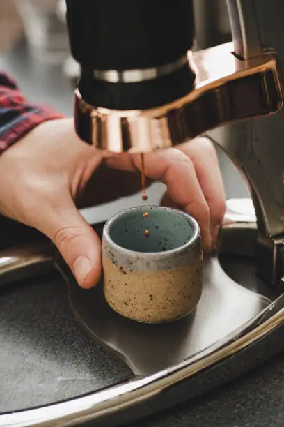 hand holding blue ceramic mug under maual espresso machine with coffee dripping close up