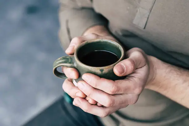 landscape close up soft focus image of mans hands holding black coffee in olive green natural ceramic mug with neutral tones and soft background