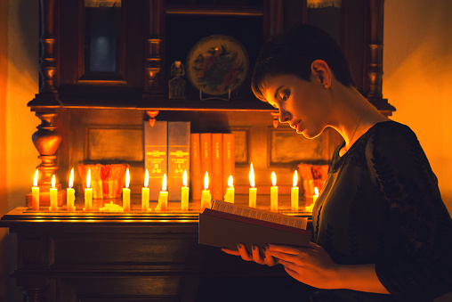 Beautiful young woman reading the book under the candlelight.