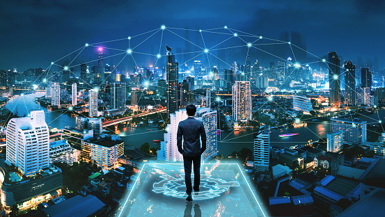 Business smart city technology concept, Professional business man walking on futuristic network city background and futuristic interface graphic at night in Bangkok, Thailand, Panorama view
