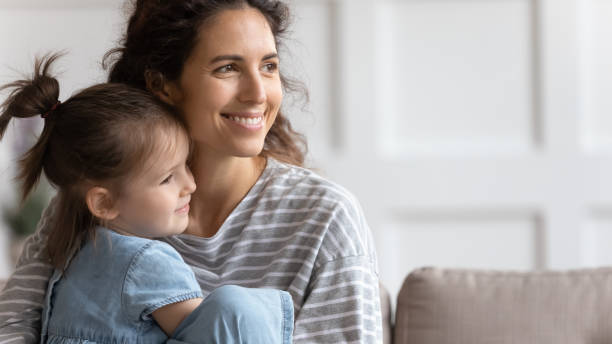 istock Mother and little daughter sit on sofa smiling looking away 1270939859
