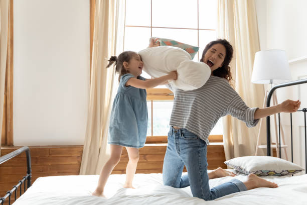 母娘は寝室で面白い時間を過ごす戦い枕を保持しています - pillow child play family ストックフォトと画像
