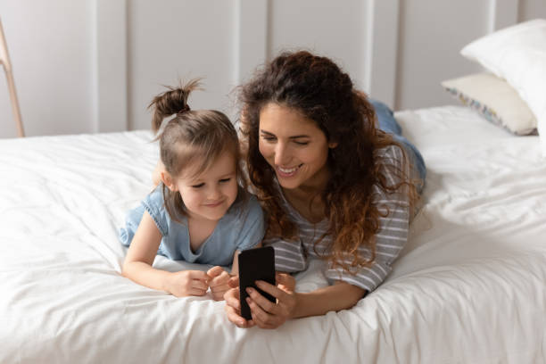 istock Mother lying on bed with daughter having fun using smartphone 1270939940