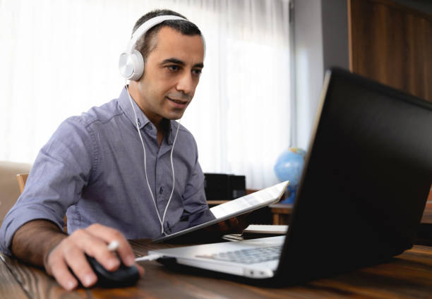 istock Man Is Working Online In Home Office Using His Laptop Computer, Joining Webinar And Taking Notes On Digital Tablet 1270941245
