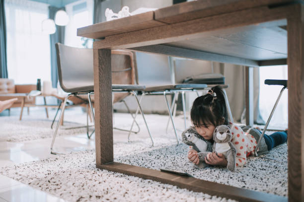 asian chinese yuoung girl hiding under dining table using her smart phone watching online show program