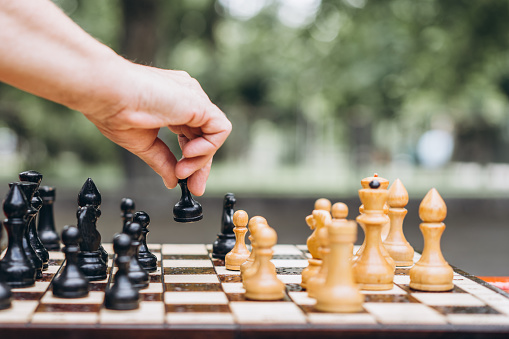 Close up of senior adult menâs hand playing chess on the bench outdoors in the park