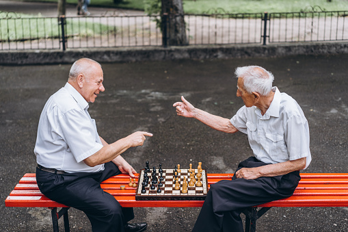 Two senior adult men playing chess on the bench outdoors in the park