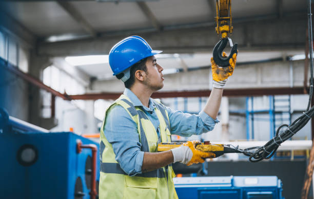 Young businessman holding and working with remote control for operating crane Young heavy industry worker man holding crane hook button working with safety workwear and moving a massive metal construction object in warehouse of factory. XXXL size hook equipment stock pictures, royalty-free photos & images