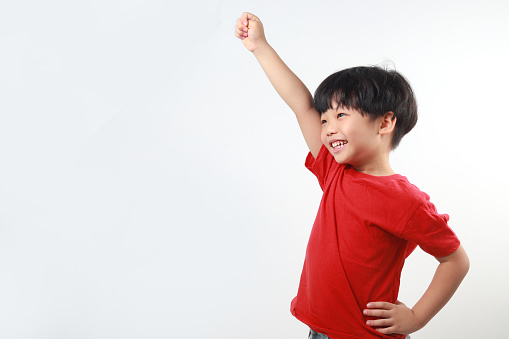 Smiling little Asian boy raising hand, looking away against white background