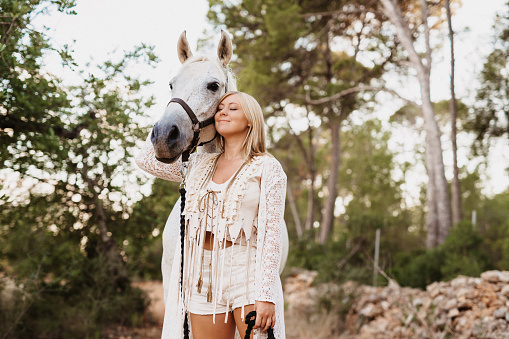 Blonde young woman with her white horse in nature in Majorca