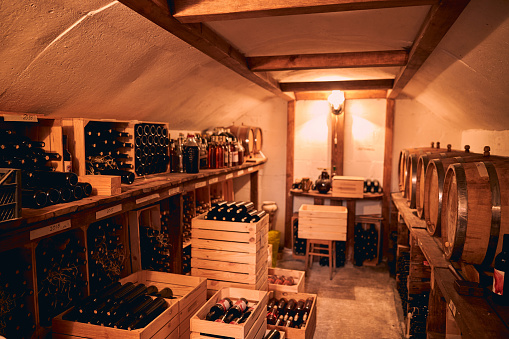 Wine cellar with bottles of alcoholic drink in wooden crates and barrels on wooden stands