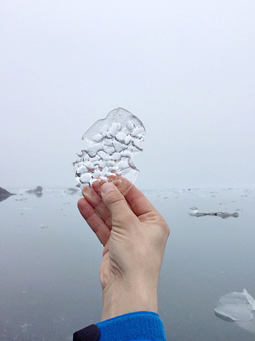 A fleeting piece of ice held in the hand in the foreground. It's a foggy weather and no view of the glacier in the background.