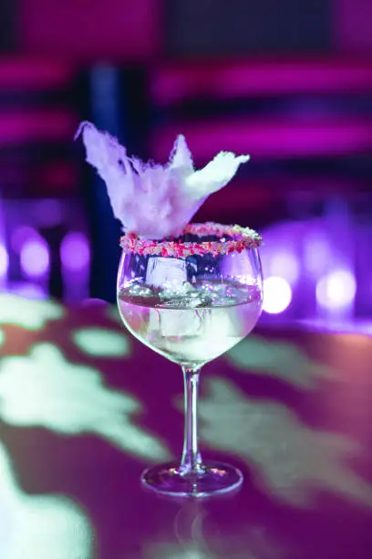 vertical image with blured background of a single cocktail with sugared rim and candy floss