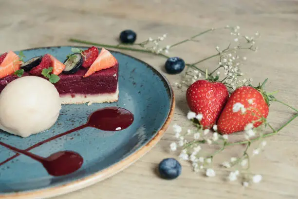 close up landscape shot of a plated strawberry slice dessert with sorbet, on a blue plate and pale wood backdrop, with elderflower, lime, strawberries and blueberries
