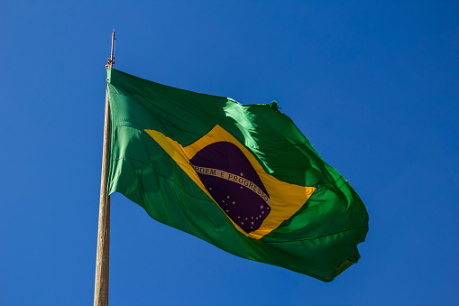 Flag of Brazil hoisted fluttering in the wind and with blue sky in the background.