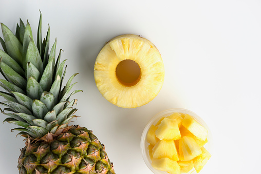 Top view of fresh pineapple with tropical monstera leaves on gray background.