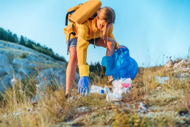 Young caucasian woman activist picking up trash in nature