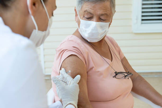 Vaccination Senior woman wearing a protective face mask is getting vaccination from a female doctor with white surgical gloves and protective face mask. tetanus photos stock pictures, royalty-free photos & images