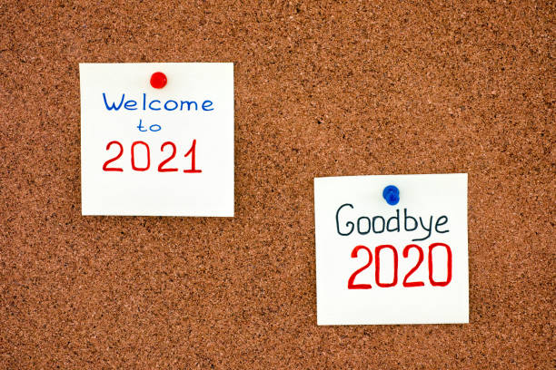 Two notes with phrases Goodbye 2020 and Welcome to 2021 on corkboard